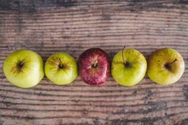 Ortasında bir kırmızı elma olan bir grup yeşil elma, sağlıklı yiyecek kavramı veya kalabalıktan dikkat çekme metaforu.