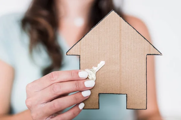 real estate and first time home buyers concept, woman holding cardboard house icon and key towards the camera