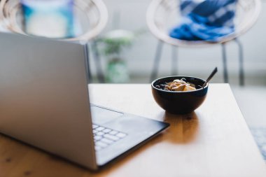 Evde dizüstü bilgisayarla çalışırken mango yulaf ezmesi yemek, uzaktan kumanda konsepti ya da ofiste öğle yemeği yemek.