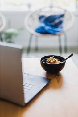 Evde dizüstü bilgisayarla çalışırken mango yulaf ezmesi yemek, uzaktan kumanda konsepti ya da ofiste öğle yemeği yemek.