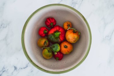 Meyve kâsesinde taze toplanmış dolmalık biber ve farklı renklerde domatesler. Basit, sağlıklı malzemeler kavramı.