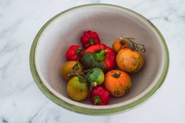 Meyve kâsesinde taze toplanmış dolmalık biber ve farklı renklerde domatesler. Basit, sağlıklı malzemeler kavramı.