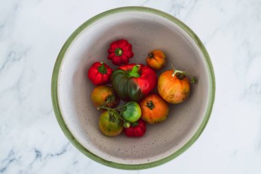 Meyve kâsesinde taze toplanmış dolmalık biber ve farklı renklerde domatesler. Basit, sağlıklı malzemeler kavramı.