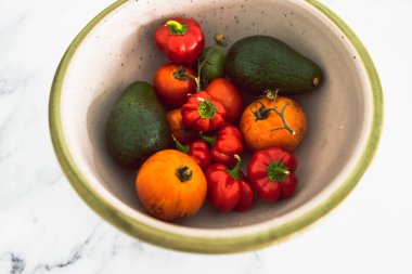 Taze toplanmış domatesli meyve kasesi aocados ve mini dolmalık biber, basit doğal sağlıklı malzemeler konsepti.