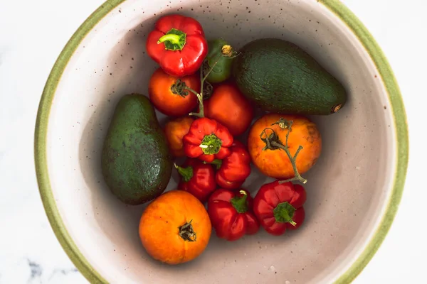 Taze toplanmış domatesli meyve kasesi aocados ve mini dolmalık biber, basit doğal sağlıklı malzemeler konsepti.