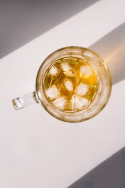 Kahverengi ya da kehribar bardakta altın rengi likör beyaz zemin üzerinde buz ve yukarıdan aşağıya doğru sert güneş ışığı vuruşu.