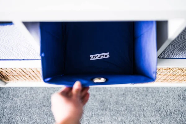 İçinde Declutter etiketi olan el kutusunu almak ve arka planda başka sepetler bulunan odaksız depolama dolabı, evinizi düzenleme ve azaltma kavramı