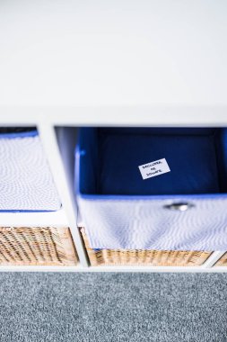 Dornatif etiketli bir depolama küpü. Arka planda başka sepetler bulunan odaksız bir depolama dolabı. Evinizi düzenleme ve küçültme kavramı.