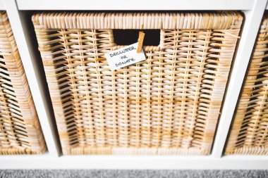 Üzerinde Declutter ya da Bağış etiketi olan sepetin üzerinde odaklanmamış depolama dolabı ve arka plandaki diğer sepetler, evinizi küçültme ve düzenleme kavramı