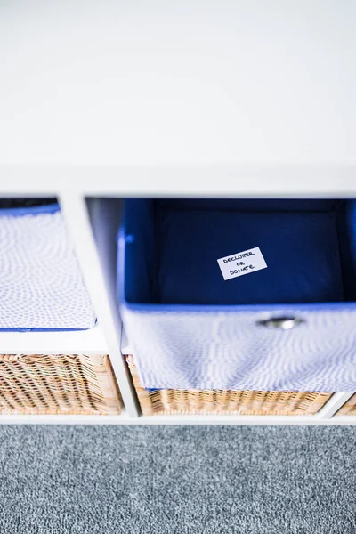 Dornatif etiketli bir depolama küpü. Arka planda başka sepetler bulunan odaksız bir depolama dolabı. Evinizi düzenleme ve küçültme kavramı.