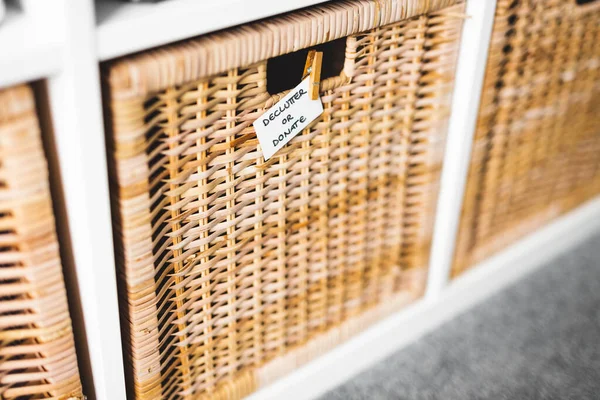 Üzerinde Declutter ya da Bağış etiketi olan sepetin üzerinde odaklanmamış depolama dolabı ve arka plandaki diğer sepetler, evinizi küçültme ve düzenleme kavramı