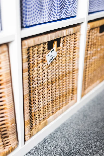 Üzerinde Declutter ya da Bağış etiketi olan sepetin üzerinde odaklanmamış depolama dolabı ve arka plandaki diğer sepetler, evinizi küçültme ve düzenleme kavramı