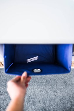 İçinde Declutter etiketi olan el kutusunu almak ve arka planda başka sepetler bulunan odaksız depolama dolabı, evinizi düzenleme ve azaltma kavramı