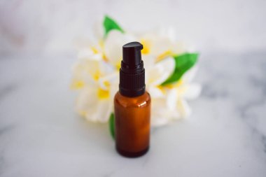 Doğal güzellik ve organik malzemeler cilt bakımı, eczacı derisi şişesi ve arka planda tropikal frangipani çiçekleri.