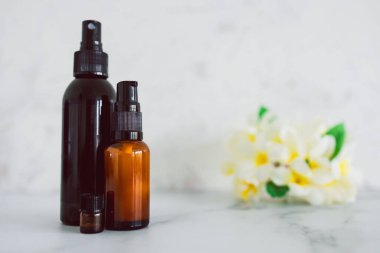 Cilt bakımındaki doğal güzellik ve organik malzemeler, arka planda tropikal frangipani çiçekleri olan eczacı derisi şişeleri.