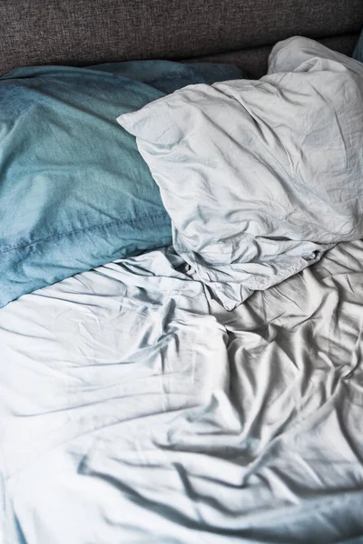 messy bed with light blue quilt cover and sheets looking crumpled and untidy, lack of sleep or bad sleep quality concept