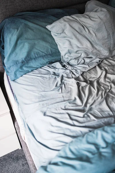 messy bed with light blue quilt cover and sheets looking crumpled and untidy, lack of sleep or bad sleep quality concept