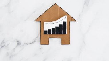 konut kredileri ve emlak fiyatlarının artması ve düşmesi, kartondan yapılmış ev ikonu ve yükselen istatistikleri gösteren grafikler