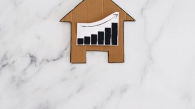 konut kredileri ve emlak fiyatlarının artması ve düşmesi, kartondan yapılmış ev ikonu ve yükselen istatistikleri gösteren grafikler