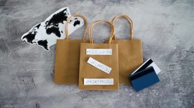 Dünya haritası ve ödeme kartlarının bulunduğu alışveriş torbaları üzerinde covid kavramsal imaj, enflasyon kıtlığı ve durgunluk metinlerinin ardından ekonomi