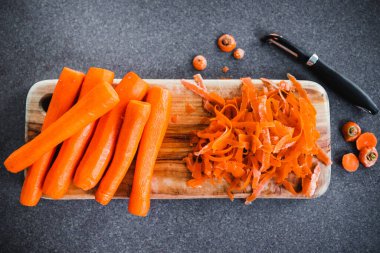 Tahta kesim tahtasının üzerine taze havuç kabuğu soyuluyor. Basit, sağlıklı malzemeler kavramı.