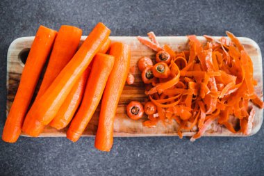 Tahta kesim tahtasının üzerine taze havuç kabuğu soyuluyor. Basit, sağlıklı malzemeler kavramı.