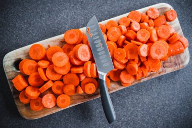 Yakın plan taze havuç dilimlenir tahta kesme tahtasının ortasında bıçak, basit doğal sağlıklı malzemeler konsepti