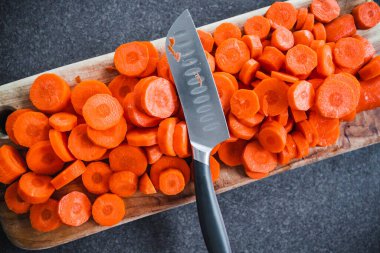 Yakın plan taze havuç dilimlenir tahta kesme tahtasının ortasında bıçak, basit doğal sağlıklı malzemeler konsepti