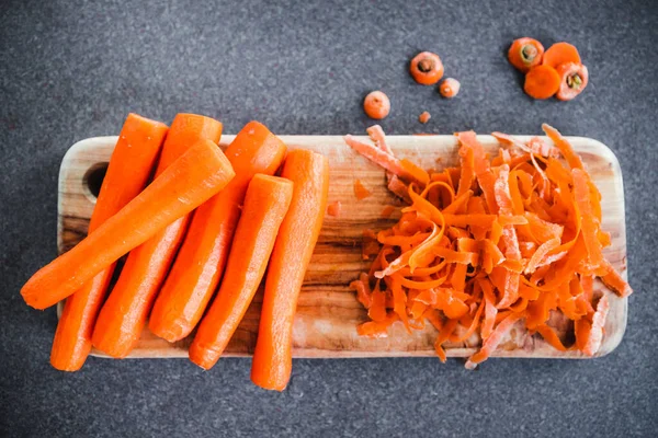 Tahta kesim tahtasının üzerine taze havuç kabuğu soyuluyor. Basit, sağlıklı malzemeler kavramı.