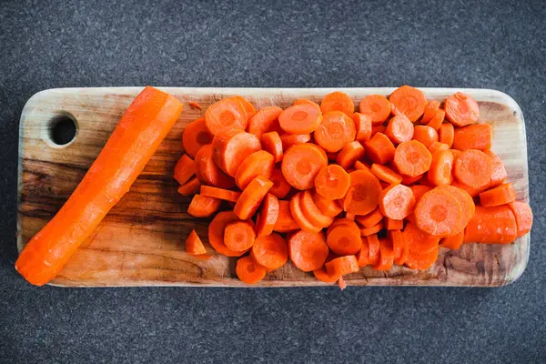 Tahta doğrama tahtasının üzerinde taze havuçların dilimlendiği yakın plan çekimler, basit, sağlıklı malzemeler kavramı.