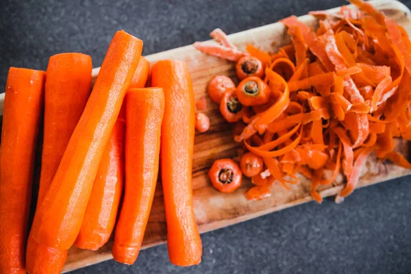 Tahta kesim tahtasının üzerine taze havuç kabuğu soyuluyor. Basit, sağlıklı malzemeler kavramı.