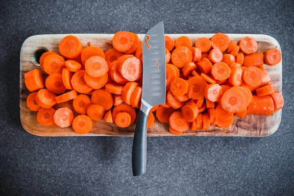 Yakın plan taze havuç dilimlenir tahta kesme tahtasının ortasında bıçak, basit doğal sağlıklı malzemeler konsepti