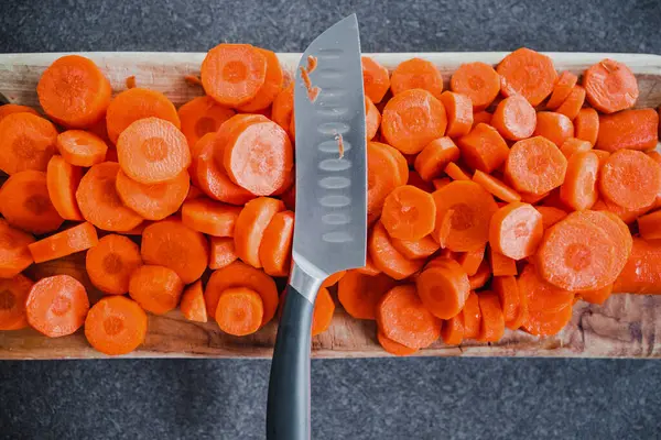 Yakın plan taze havuç dilimlenir tahta kesme tahtasının ortasında bıçak, basit doğal sağlıklı malzemeler konsepti