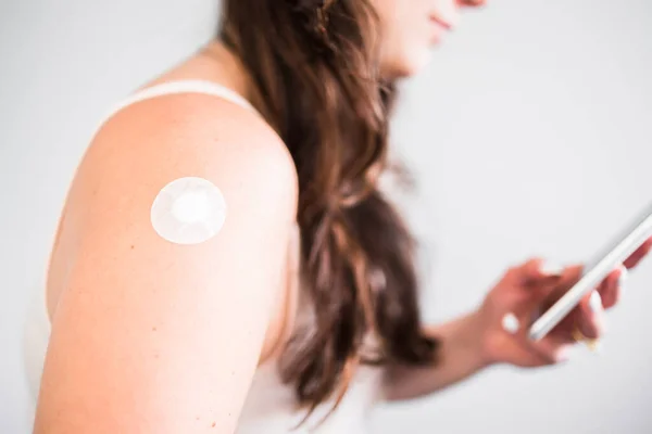 woman showing covid-19 or flu vaccination band-aid on her arm while looking at her phone, concept of protection from the pandemic and and seasonal viruses like influenza