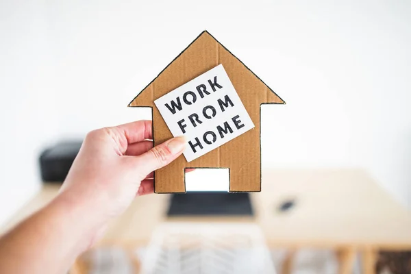 work from home sign being hold in front of out of focus home office desk setup, concept of digital nomads working remotely or wfh days during lockdowns or covid-19 isolation