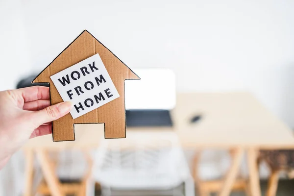 work from home sign being hold in front of out of focus home office desk setup, concept of digital nomads working remotely or wfh days during lockdowns or covid-19 isolation