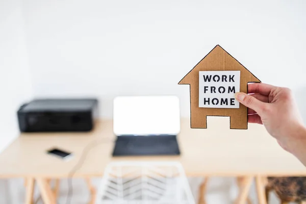 work from home sign being hold in front of out of focus home office desk setup, concept of digital nomads working remotely or wfh days during lockdowns or covid-19 isolation