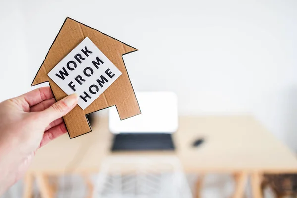 work from home sign being hold in front of out of focus home office desk setup, concept of digital nomads working remotely or wfh days during lockdowns or covid-19 isolation