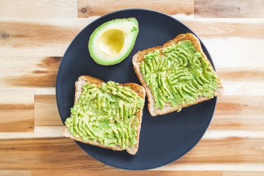 Yanında yarım avokado ve sağlıklı vejetaryen yemek tarifleri olan temel bitkisel ezilmiş avokado tostu.