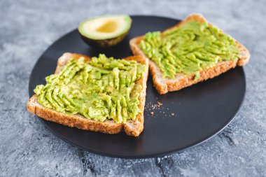 Yanında yarım avokado ve sağlıklı vejetaryen yemek tarifleri olan temel bitkisel ezilmiş avokado tostu.