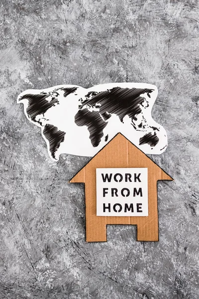 work from home sign with world map and house made of cardboard on grey background, concept of digital nomads working remotely or wfh days during lockdowns or covid-19 isolation