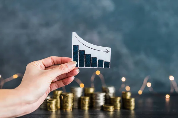 negative growth or bad business performance conceptual image, graph with negative stats in front of stacks of coins with fairy lights in the background