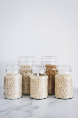 glass jar with rice of different varieties including jasmine basmati arborio sushi and brown rice, healthy pantry ingredients and staples