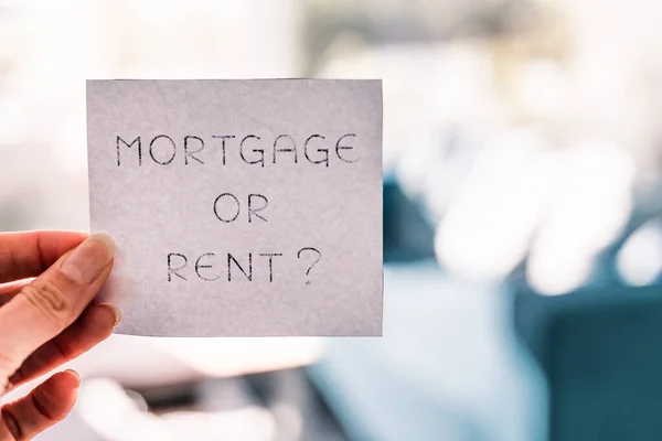 hand holding mortgage or rent sign in front of living room bokeh, concept of real estate affordability and property market