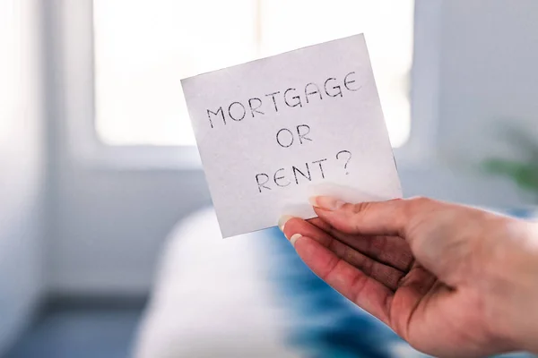 hand holding mortgage or rent sign in front of bedroom bokeh, concept of real estate affordability and property market