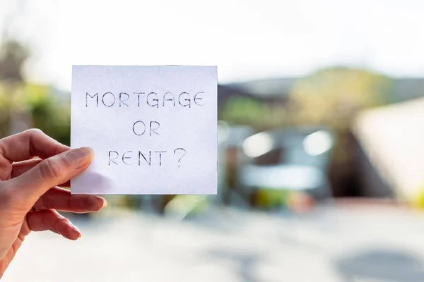 hand holding mortgage or rent sign in front of backyard bokeh, concept of real estate affordability and property market