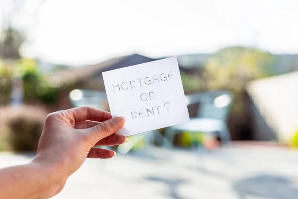 hand holding mortgage or rent sign in front of backyard bokeh, concept of real estate affordability and property market