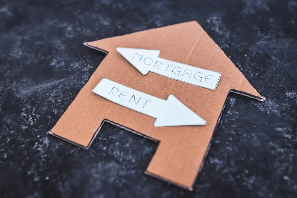 house icon with mortgage or rent signs pointing in opposite directions on dark background, concept of real estate affordability and property market