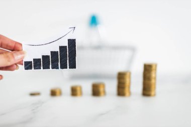 rising inflation graph in front of shopping basket and growing stacks of coins representing increasingly expensive prices, concept of global economy struggling after the covid-19 pandemic