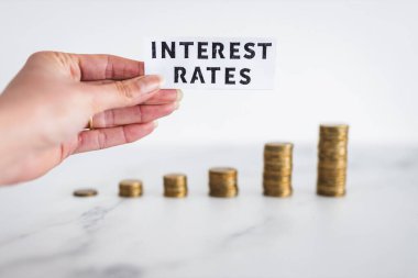 Interest Rates text with growing stacks of coins representing increasingly expensive loans and mortgages, concept of global economy struggling after the covid-19 pandemic